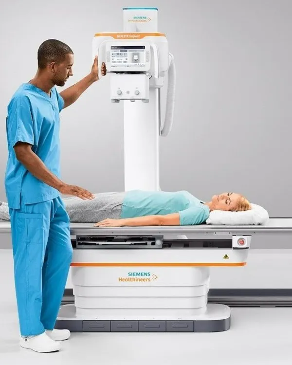 A radiographer positioning a patient on the X-ray table in the imaging room