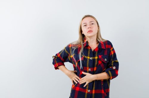 young lady in checked shirt holding hands on stomach and looking unwell , front view.